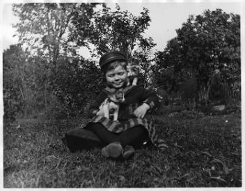 Un garçon de la famille Millard assis dans un jardin avec des chatons, Drummondville, QC, vers 1895
