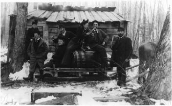 Partie de sucre, avec des personnes autour et sur un baril servant à recueillir la sève, près de Sorel (?), QC, vers 1890